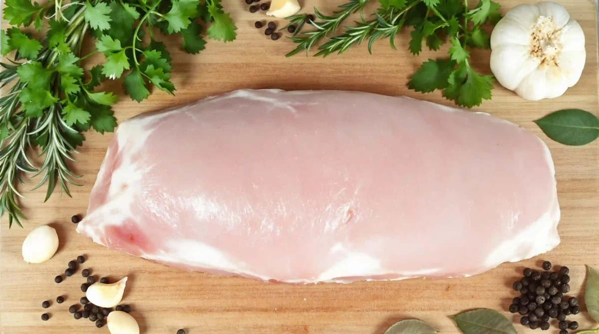 A fresh, unseasoned pork loin on a wooden cutting board, surrounded by herbs and spices. A fresh, unseasoned pork loin on a wooden cutting board, surrounded by herbs and spices.